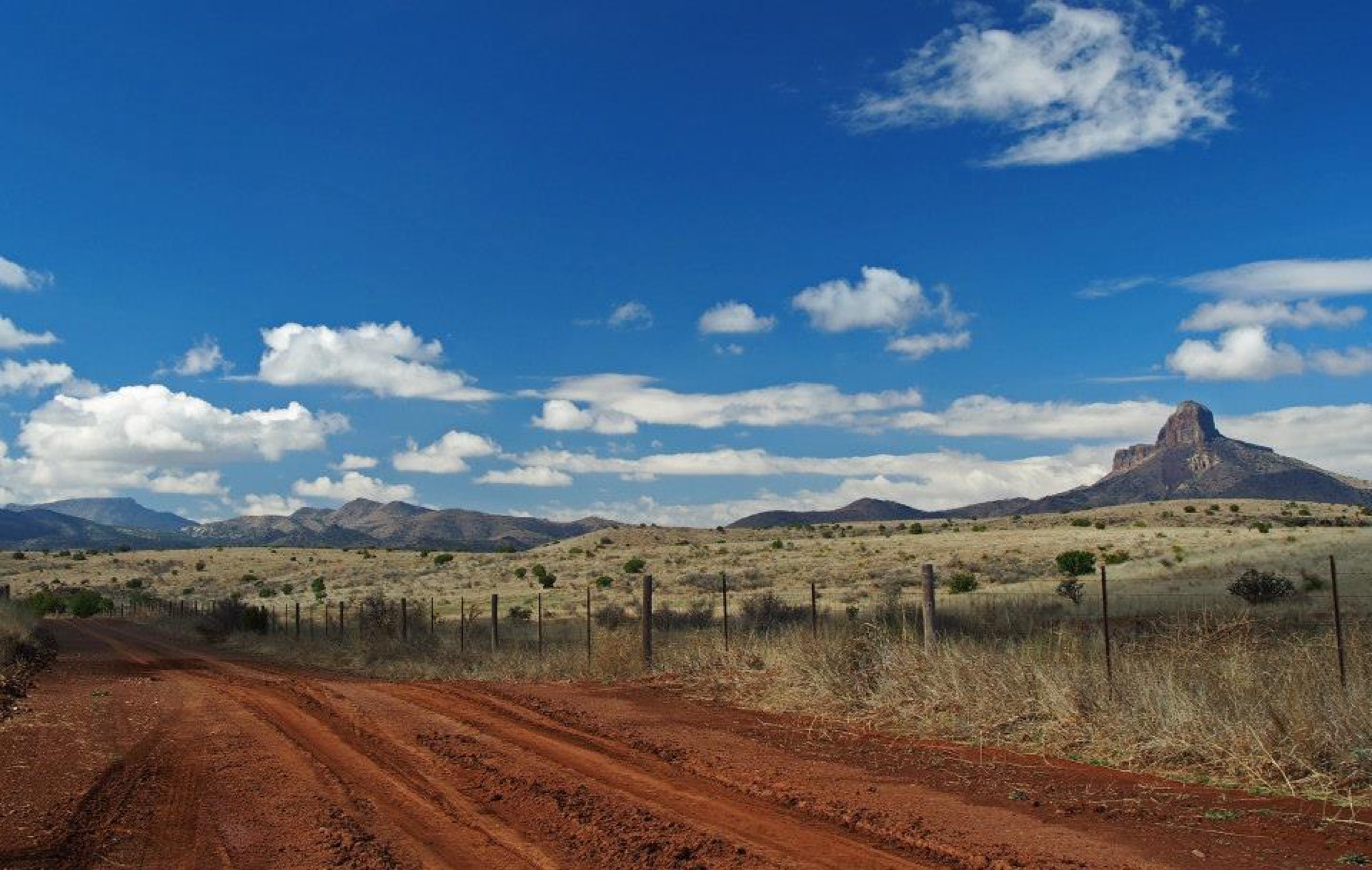 A red dirt ranch road running toward far blue mesas