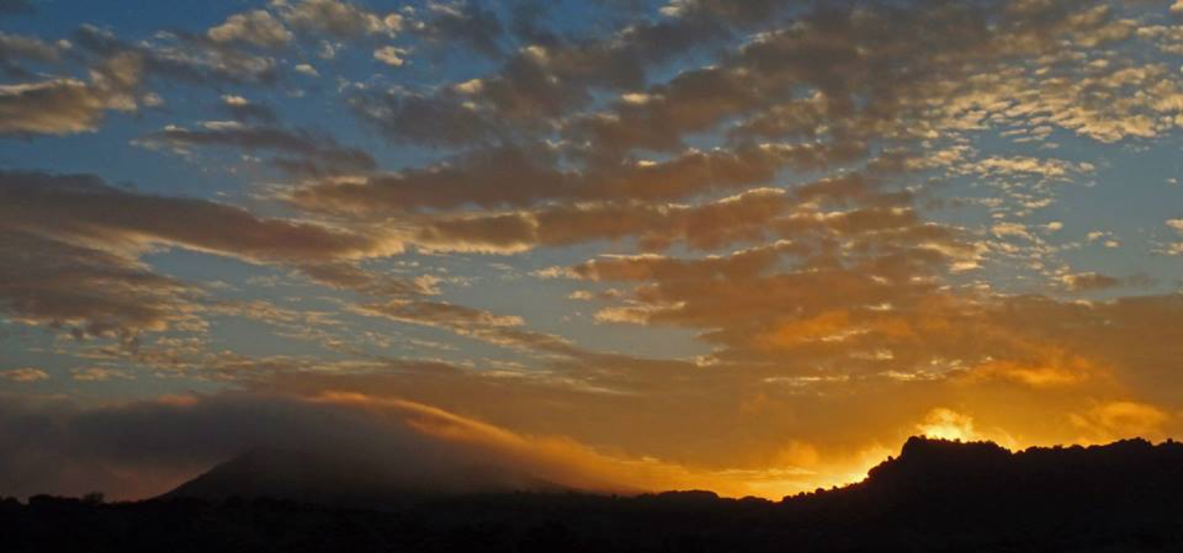 A sunset breaking under mackerel cloud over silhouetted hills