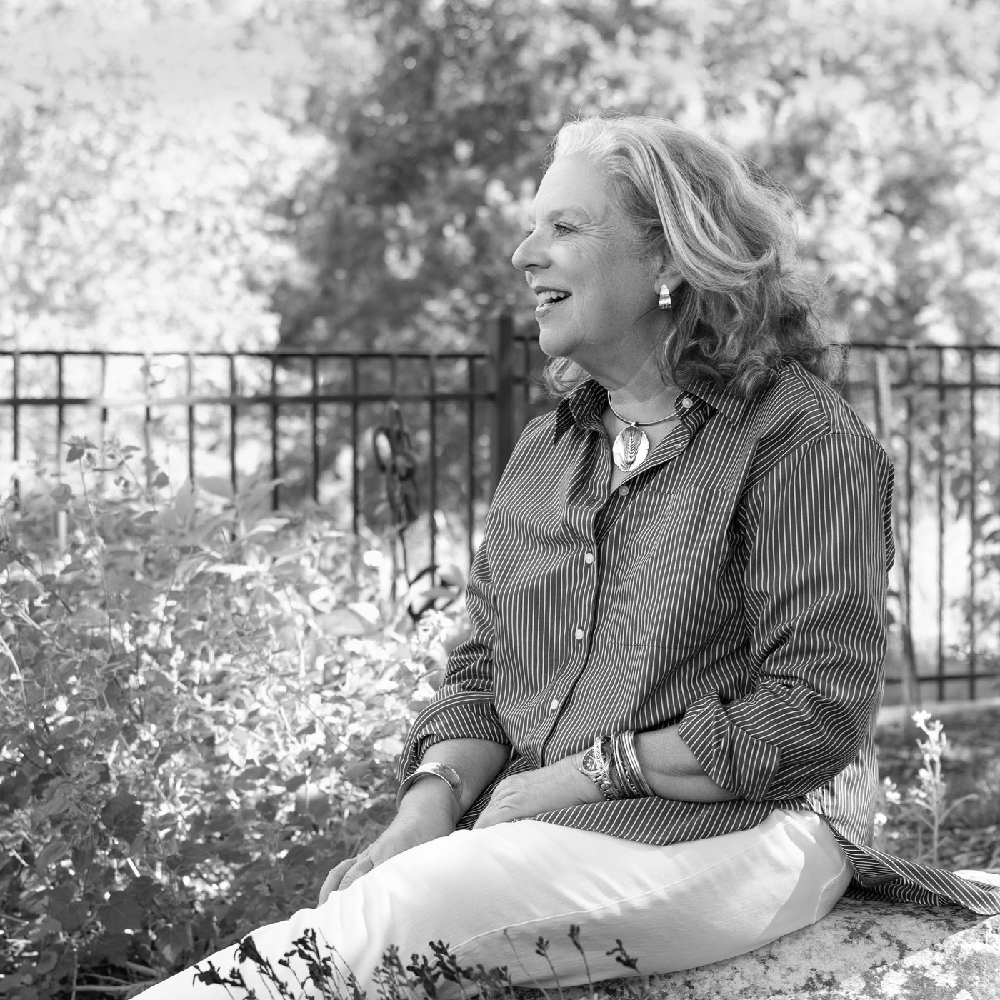 Laura in black and white, seated on a garden wall looking away toward the trees