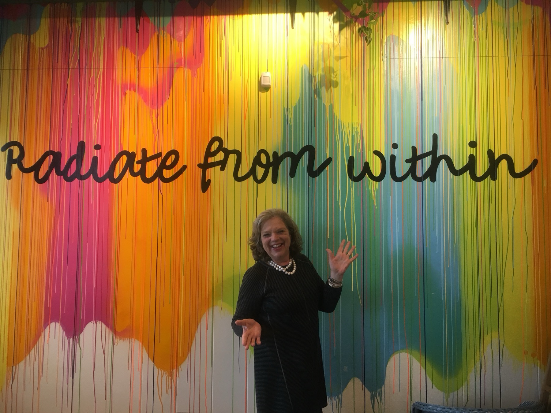 Laura in front of a painted mural reading radiate from within
