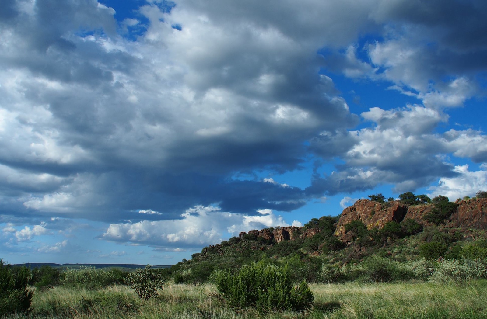 A rocky bluff standing over grassland under a sky full of cloud